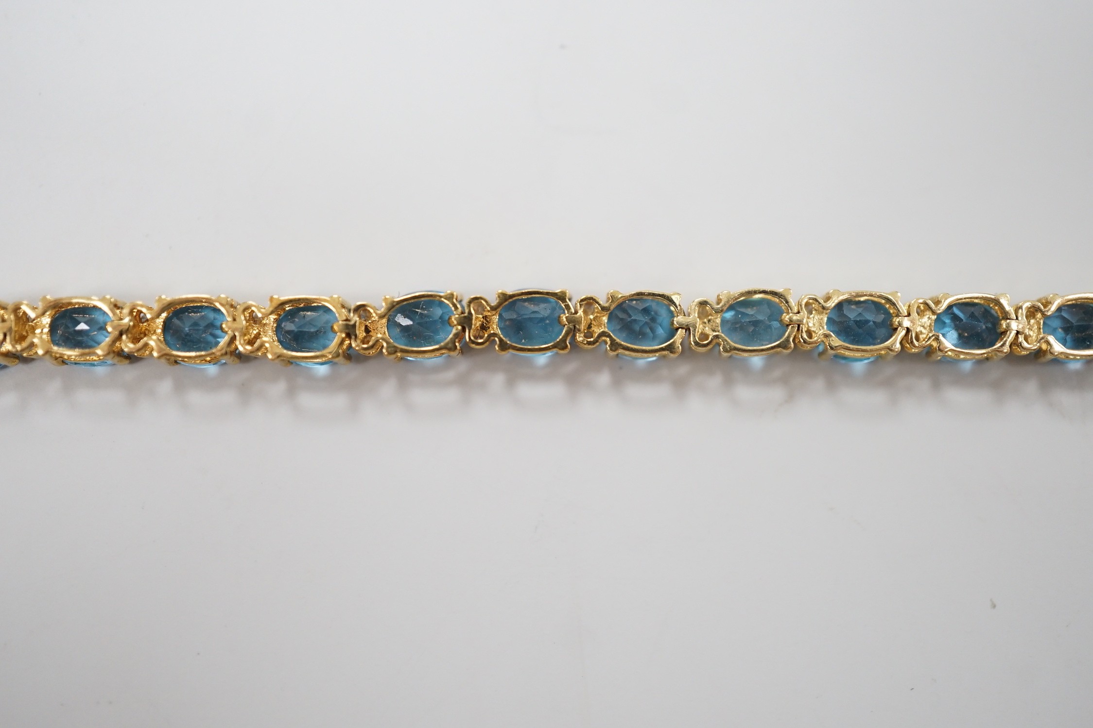 A modern 750 yellow metal and blue topaz set line bracelet, with diamond chip spacers, 17.75cm